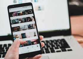 A person uses a smartphone to browse social media in front of a laptop, emphasizing modern technology and lifestyle.