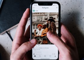 Close-up of hands holding a smartphone browsing Instagram with a notebook and pen nearby.